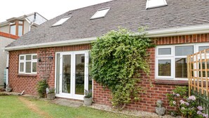 A brick house with a tiled roof, a front door, and a small garden with grass and plants. - Muskoka Lodge (Radstock)