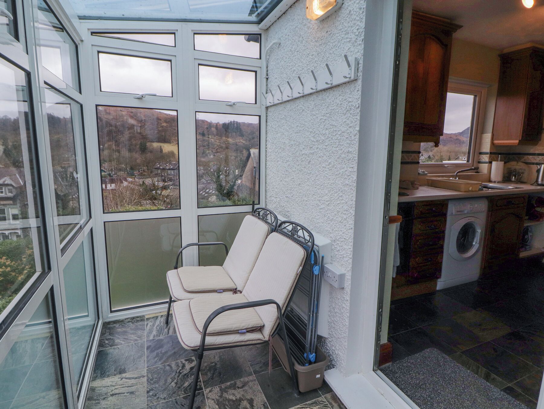 Un invernadero con vistas a un pueblo, una silla, una lavadora y una zona de cocina.
