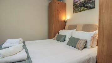 Ein ordentlich bezogenes Bett mit Kissen und einem gefalteten Handtuch, ein Holzschrank und ein Bild an der Wand.
