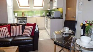 A compact living space with a sofa, a glass dining table, and a kitchenette in the background. - Bluebird Loft (Coniston)