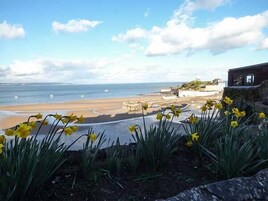 Vista costera con una playa arenosa, un muelle y un edificio con muro de piedra.