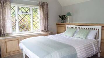 A bedroom with a bed, a window with curtains, a bedside lamp, and a view of greenery outside.
