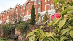 A row of red brick townhouses with white trim, a stone wall, and a bench. - 12 Deva Terrace (Chester)