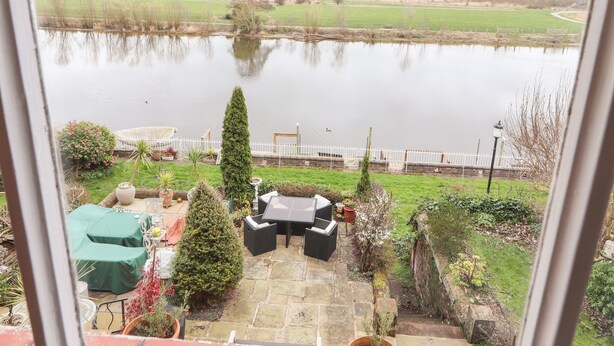 A view of a lake from a window overlooking a patio area with outdoor furniture and a small garden. - 12 Deva Terrace (Chester)