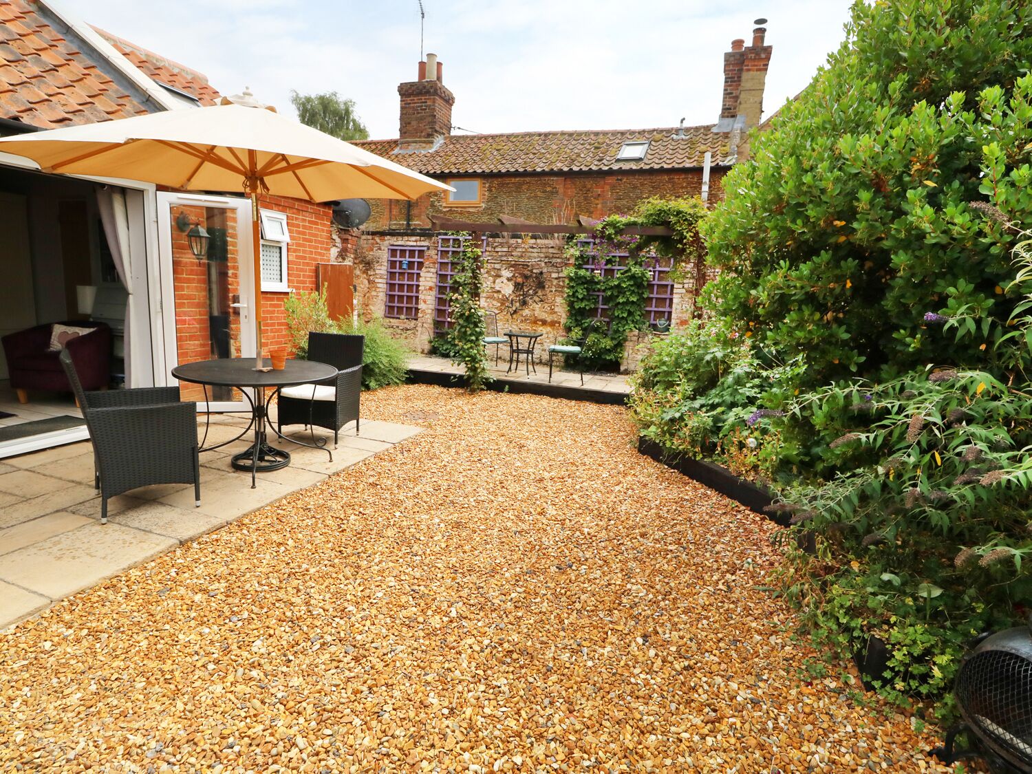Un espace patio avec une table et des chaises, un coin salon abrité et un chemin de gravier.