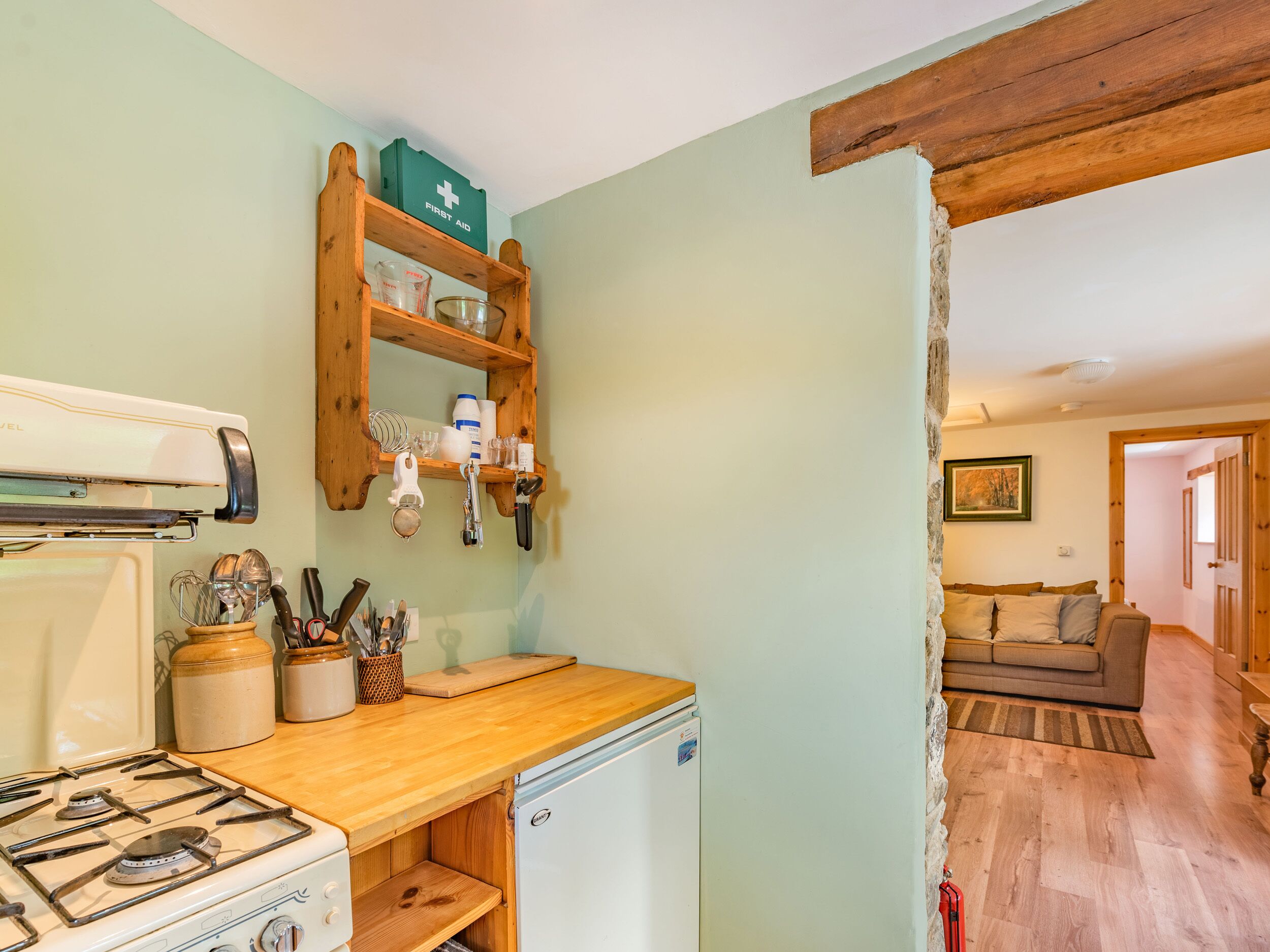 A kitchen with a gas stove, wooden countertop, and a refrigerator. There is a shelf with kitchen utensils and a first aid kit.