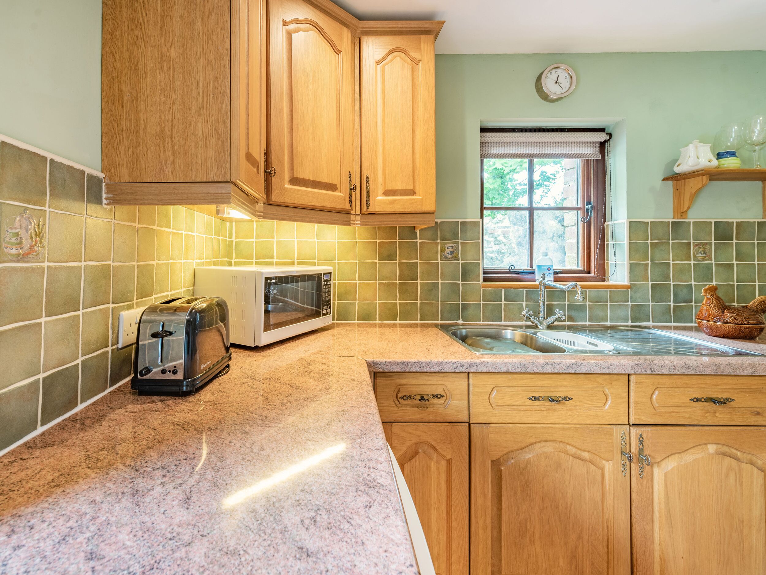 A kitchen with wooden cabinets, a microwave, a toaster, a sink, and a window with a view of greenery.