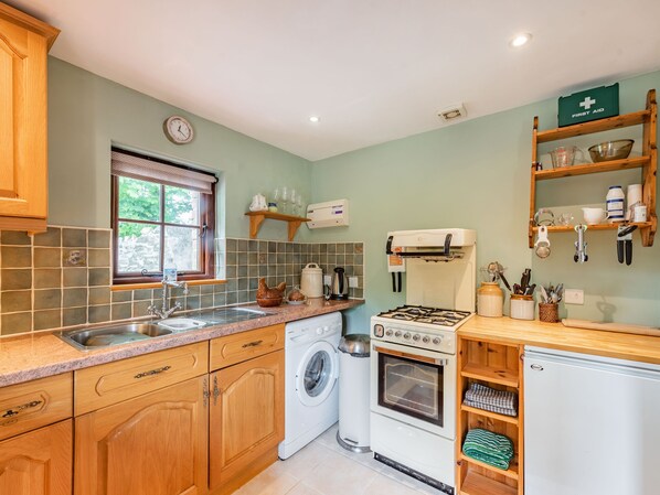 A kitchen with wooden cabinets, a washing machine, a stove, and a sink. - Cilwen Fach (Carmarthen)