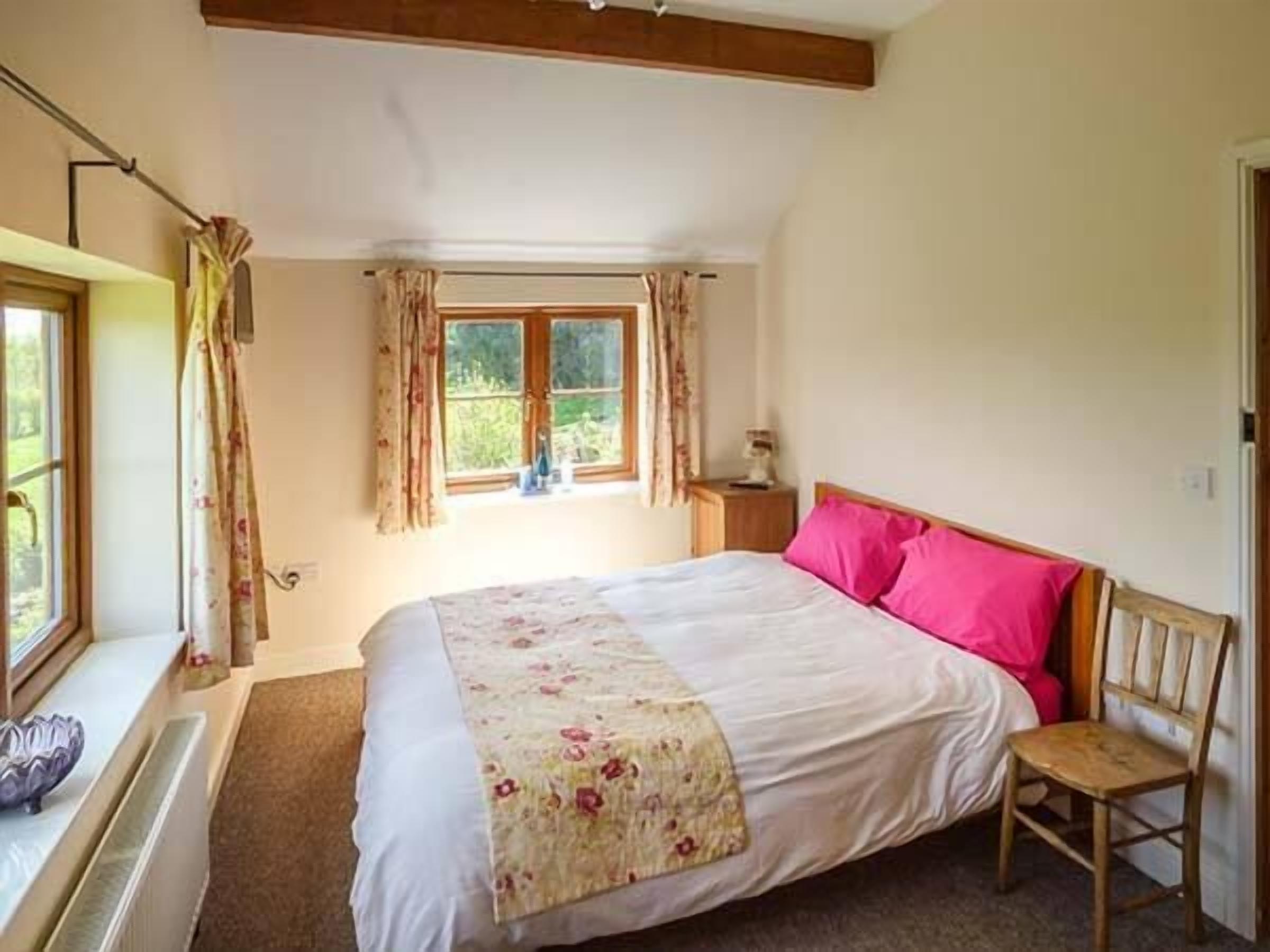 A bedroom with a bed, a chair, a window with curtains, and a radiator.