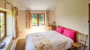 A bedroom with a bed, a chair, a window with curtains, and a radiator.
