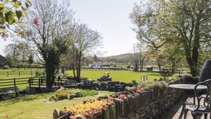 Un patio al aire libre con muros de piedra, asientos y vista a un campo verde y árboles.