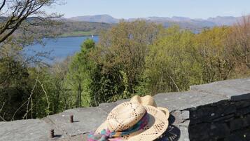 A stone wall with a straw hat and sunglasses placed on it, overlooking a lake and forested hills.