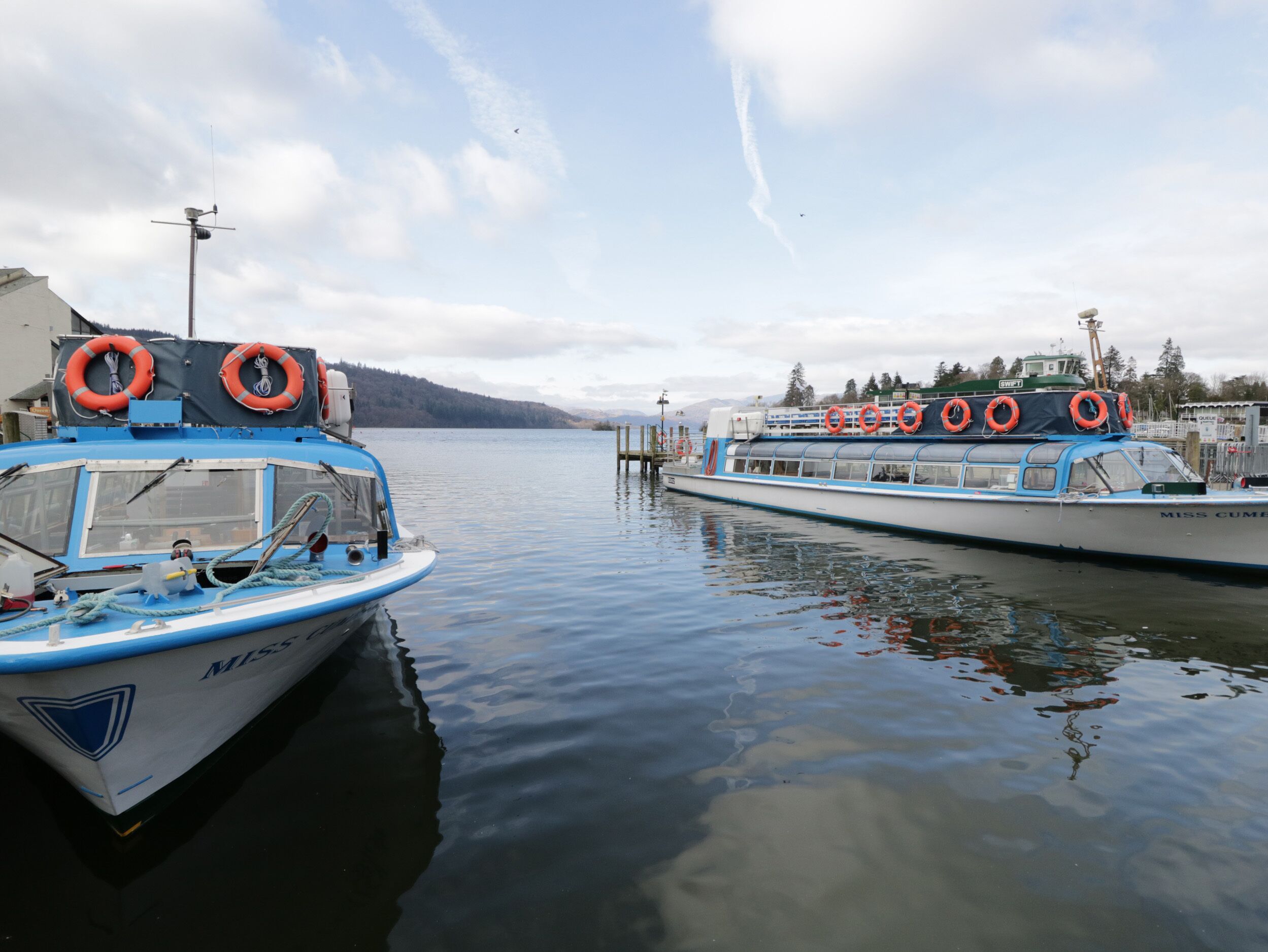 Two boats docked at a marina with lifebuoys on the side of the boats.