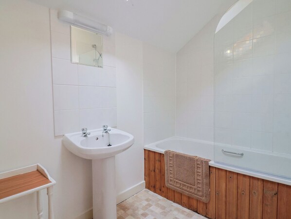 A bathroom with a white sink, a mirror, a bathtub, and wooden paneling. - West Bowden Farm (South Molton)