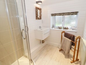 A bathroom with a glass shower enclosure, a white sink, and a window with a stone ledge. - Bron Heulog Cottage (Beaumaris)