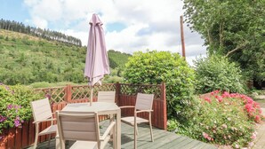 Une terrasse en bois avec une table et des chaises, entourée d’une clôture en bois et d’une végétation luxuriante.