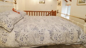 Une chambre avec un plafond en bois, un lit avec une literie à motifs, une table de chevet et une fenêtre donnant sur un paysage agréable.