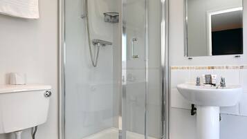 Un baño moderno con ducha de vidrio, inodoro blanco y lavamanos con espejo.