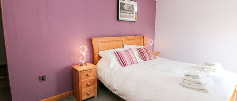 A bedroom with a wooden bed, a nightstand with a lamp, and a framed picture on the wall.