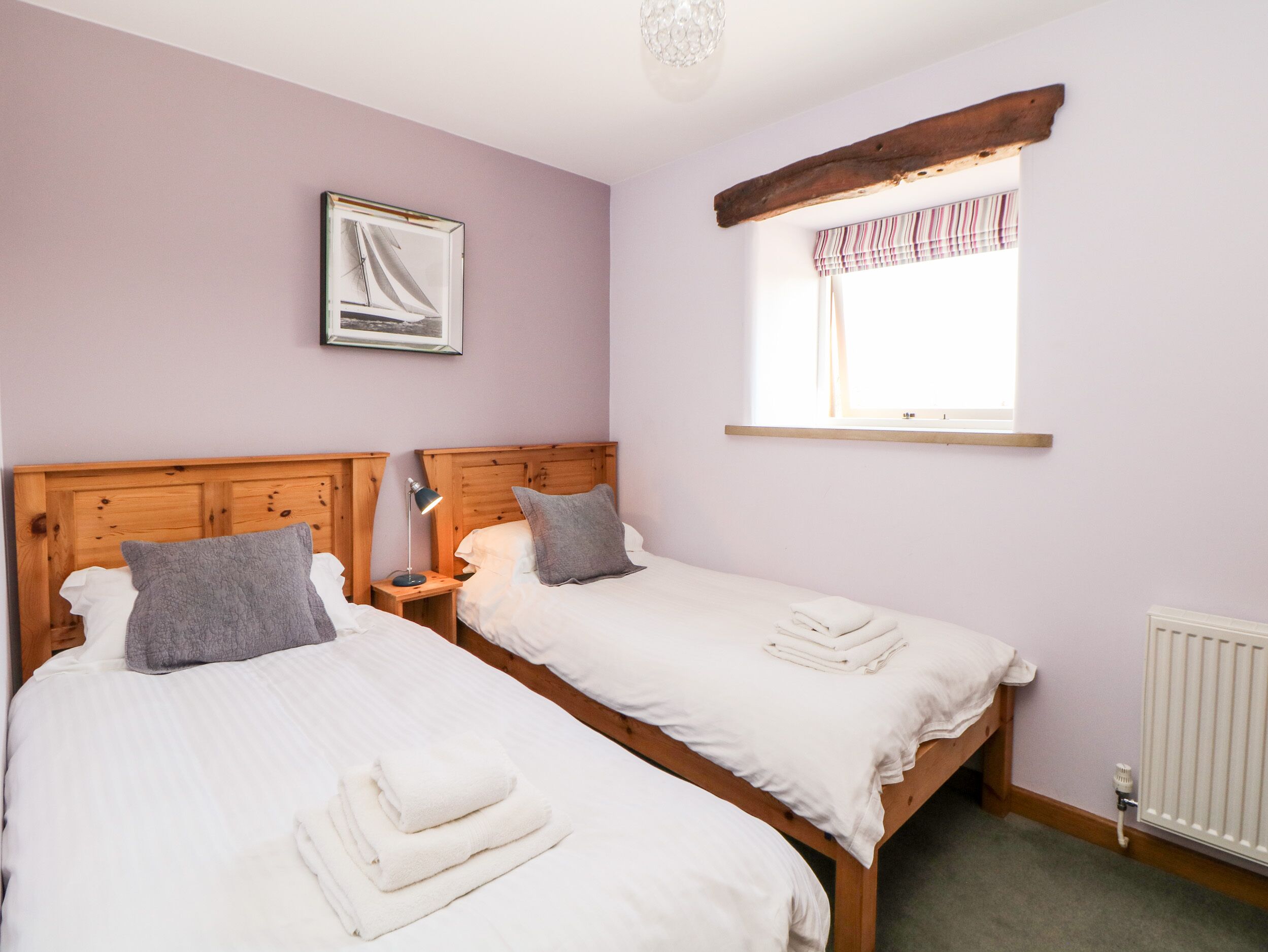A bedroom with two beds, a wooden headboard, a window with striped curtains, and a framed picture on the wall.