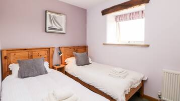 A bedroom with two beds, a wooden headboard, a window with striped curtains, and a framed picture on the wall.