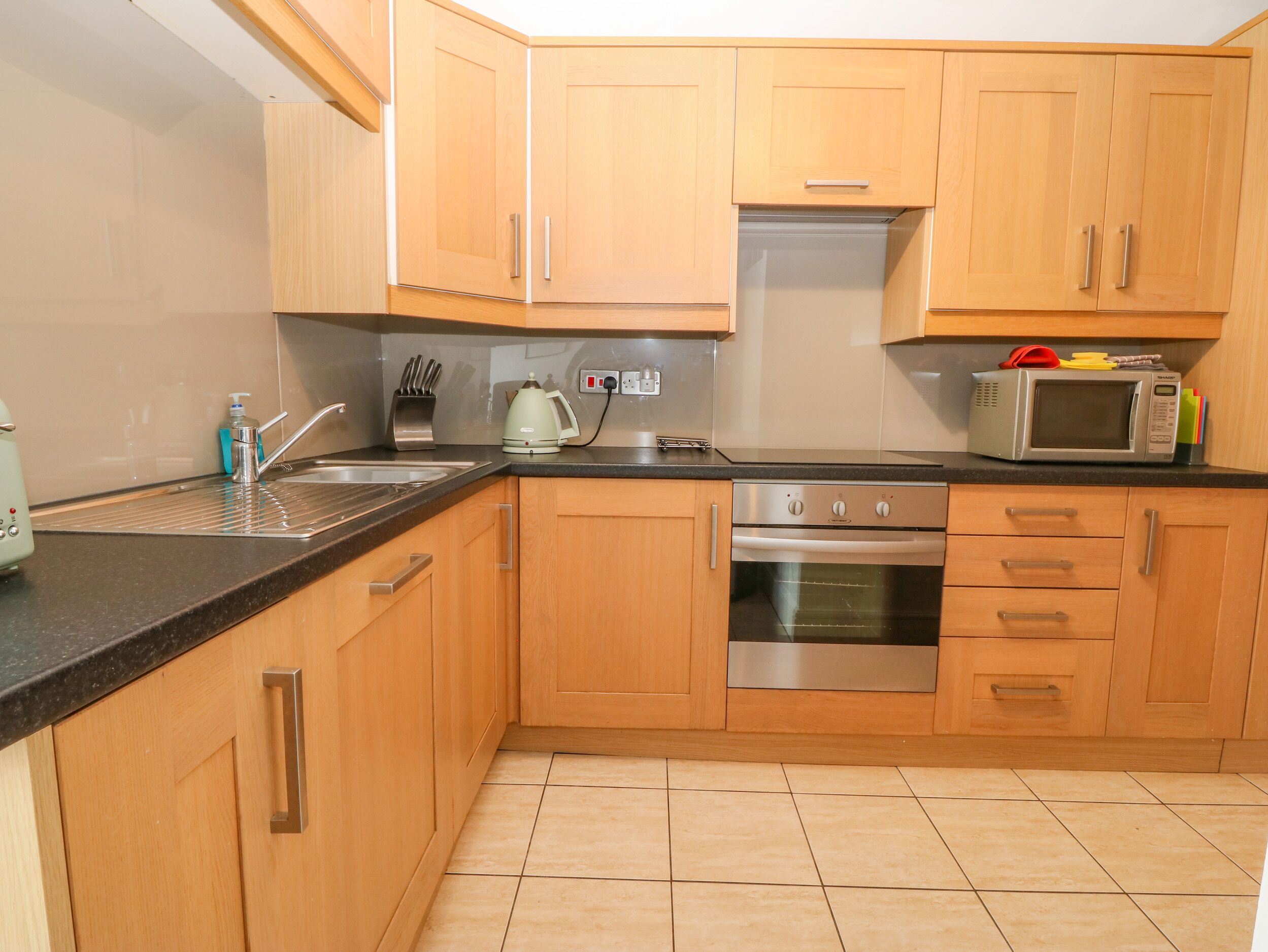 A kitchen with wooden cabinets, a stainless steel oven, a microwave, and a kettle.