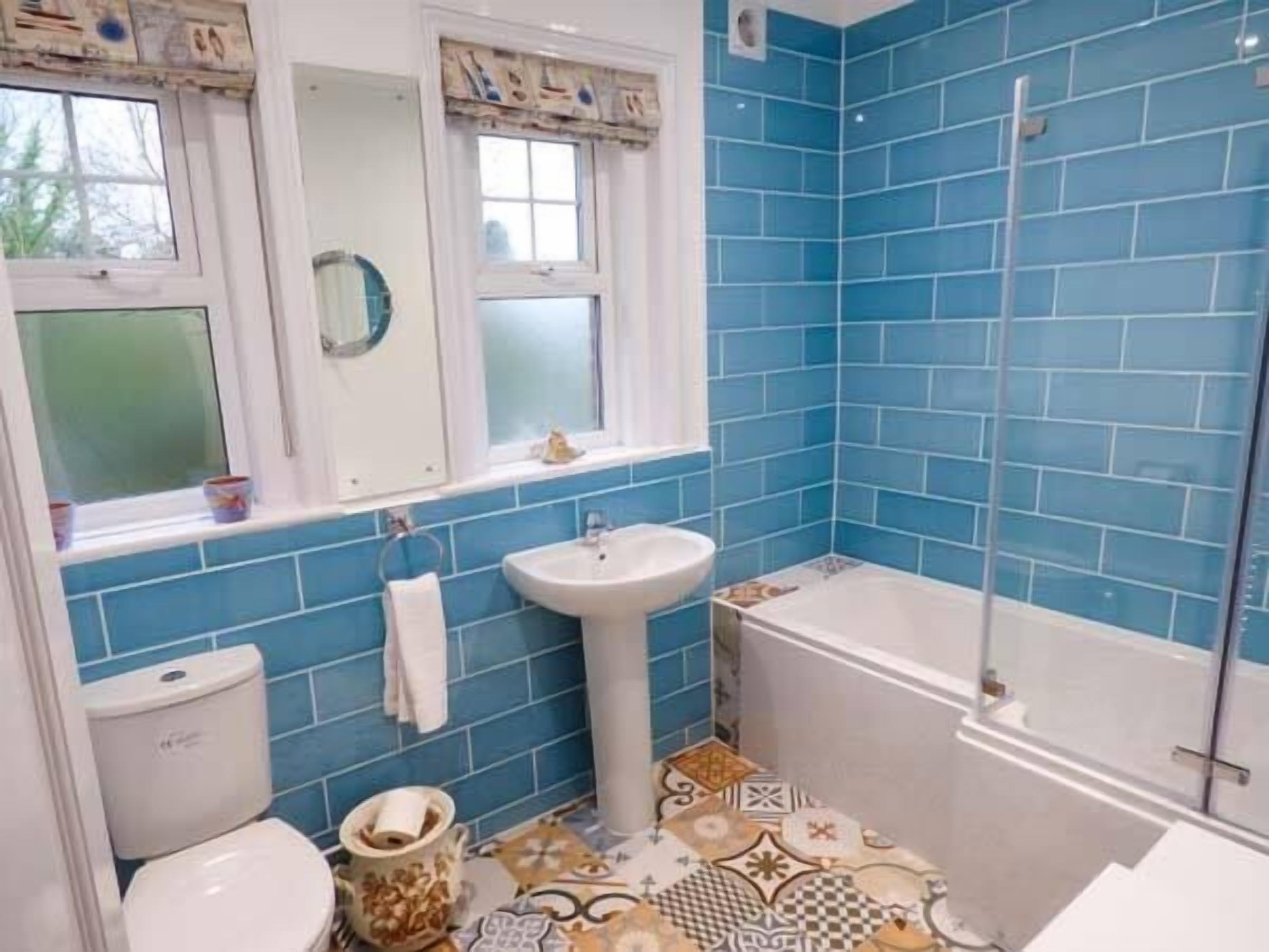 Un bany amb rajoles blaves, un lavabo blanc, un vàter i una banyera.
