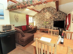 A cozy living area with a stone wall, a flat-screen TV, a wooden dining table, and a microwave. - Sonya's Cottage (Wigton)