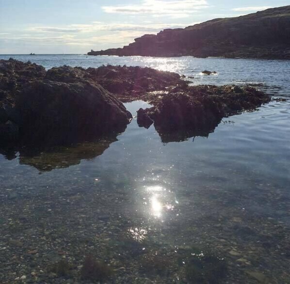 Una costa rocosa amb aigua cristal·lina que reflecteix el sol.