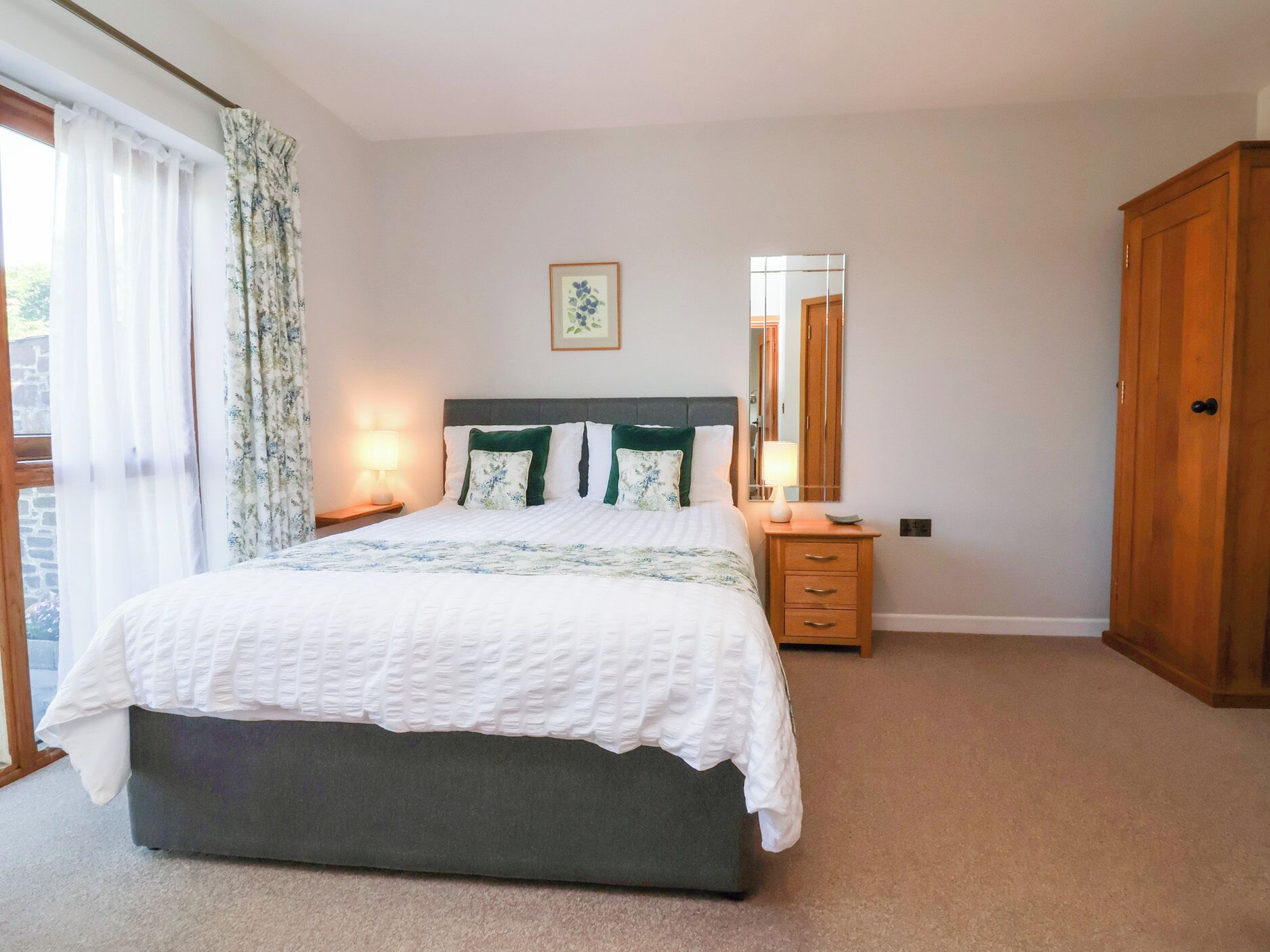 A bedroom with a bed, a nightstand, a dresser, a mirror, and a door.