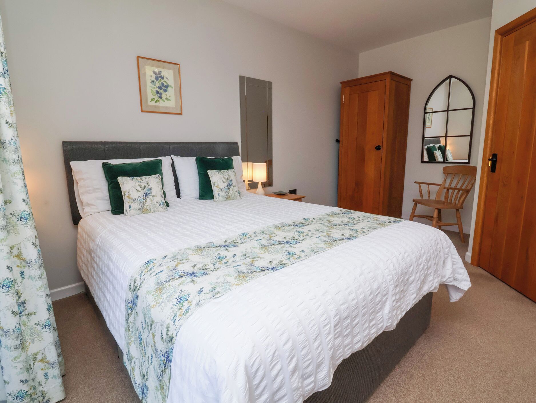 A bedroom with a large bed, a wooden wardrobe, a chair, and a framed picture on the wall.