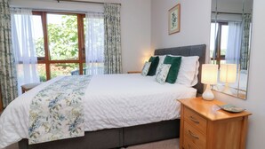 A bedroom with a bed, a nightstand, a mirror, and a window with curtains. - Pound Cottage (Torrington)