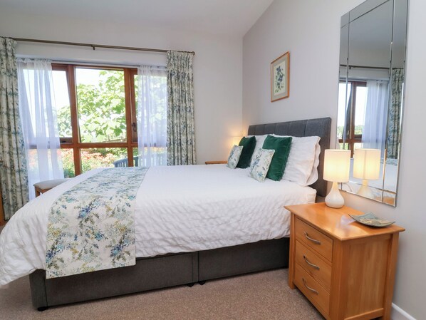 A bedroom with a bed, a nightstand, a mirror, and a window with curtains. - Pound Cottage (Torrington)