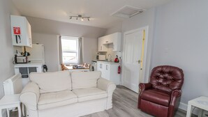 A modern living room with a sofa, a leather armchair, and a dining area with a table and chairs. - The Knowe Upper (Taynuilt)