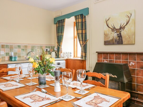A dining area with a wooden table set for a meal, a vase with flowers, and a painting of a deer on the wall.