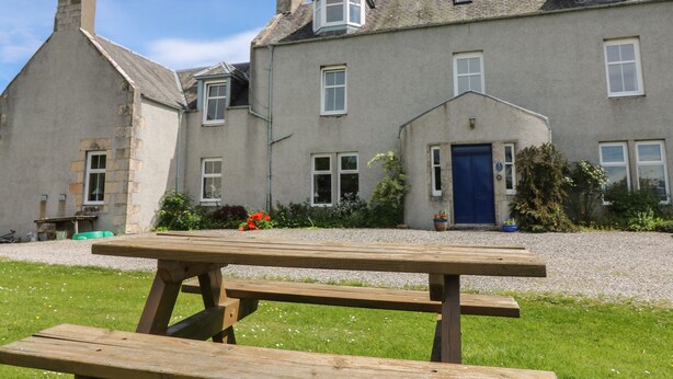 Un bâtiment traditionnel en pierre, doté d’une entrée imposante et d’une table de pique-nique en bois placée au premier plan.