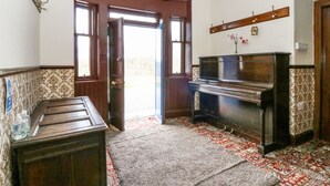 Une pièce avec un piano, un meuble en bois, une moquette à motifs et une porte donnant sur l’extérieur.