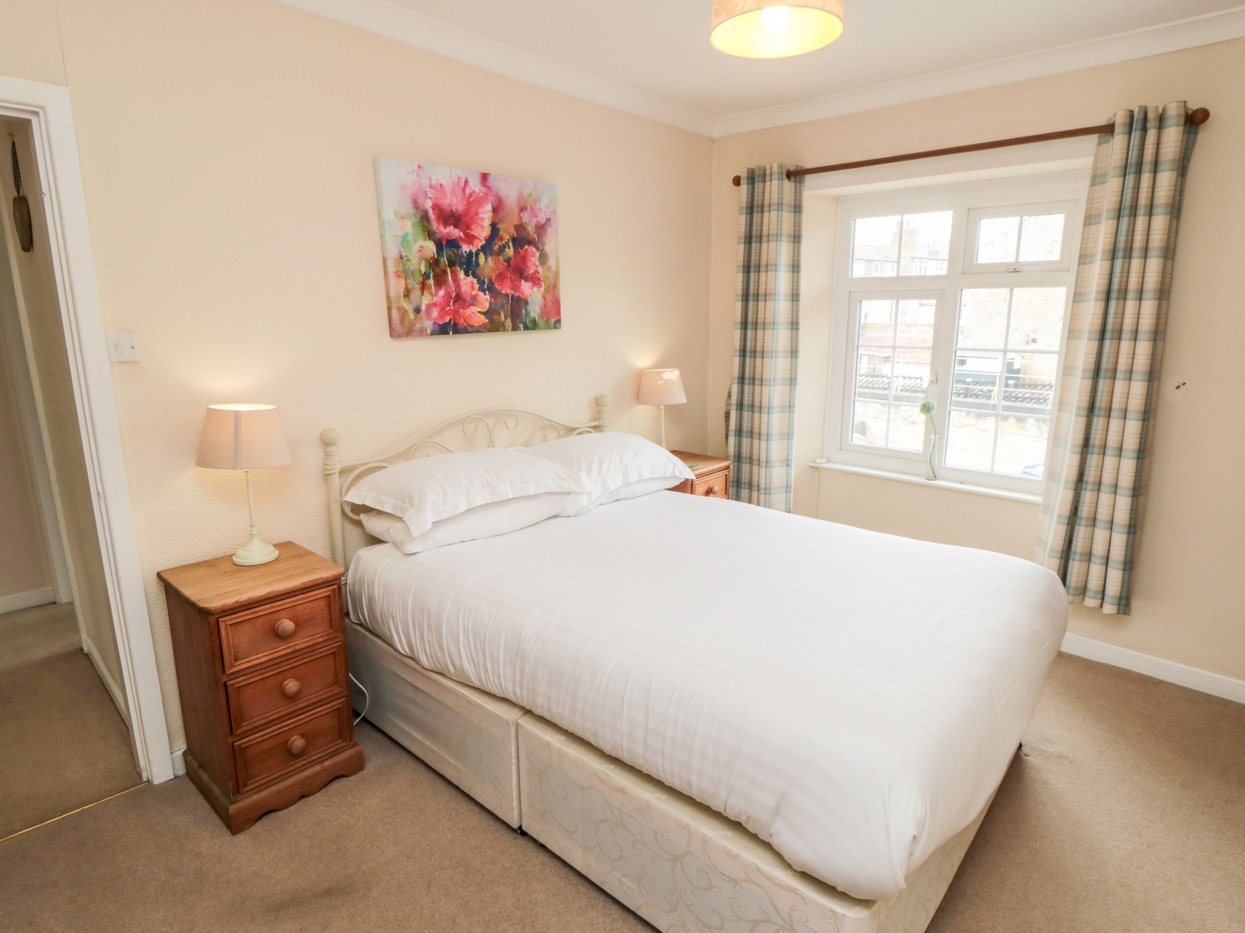 A bedroom with a bed, nightstands, a painting, a window with curtains, and a door.