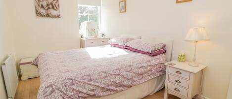 A bedroom with a bed, bedside table, lamp, dresser, and a window.