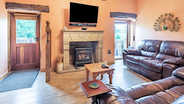A living room with a fireplace, leather sofa, and a television mounted on the wall. - Peacock Cottage (Buxton)