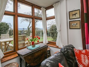 Une pièce dotée d’une grande fenêtre, d’une table en bois sur laquelle est posé un vase rempli de fleurs rouges, d’un canapé en cuir noir et de tableaux encadrés accrochés au mur.