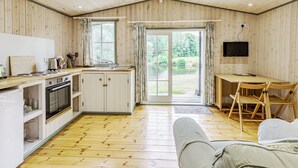 A cozy cabin interior with a kitchenette, dining area, and a large sliding glass door leading to a garden. - Lakeside Cabin (Honiton)