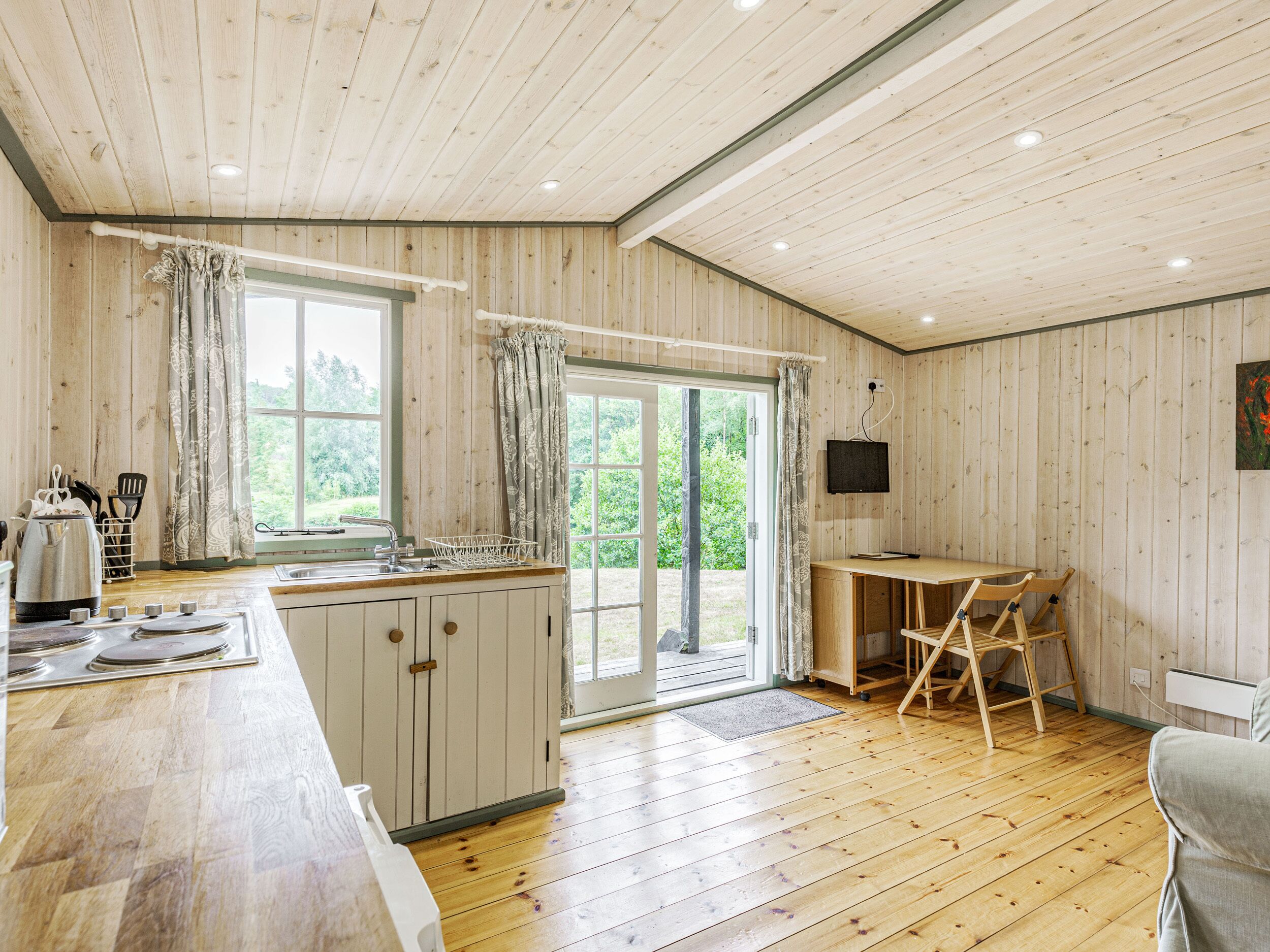 A wooden-paneled kitchen with a large window, a sink, and a dining area with a table and chairs.