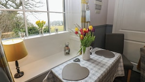 Een kamer met een gedekte tafel voor twee personen, een raam met uitzicht op bomen, en een decoratief hart aan de muur.