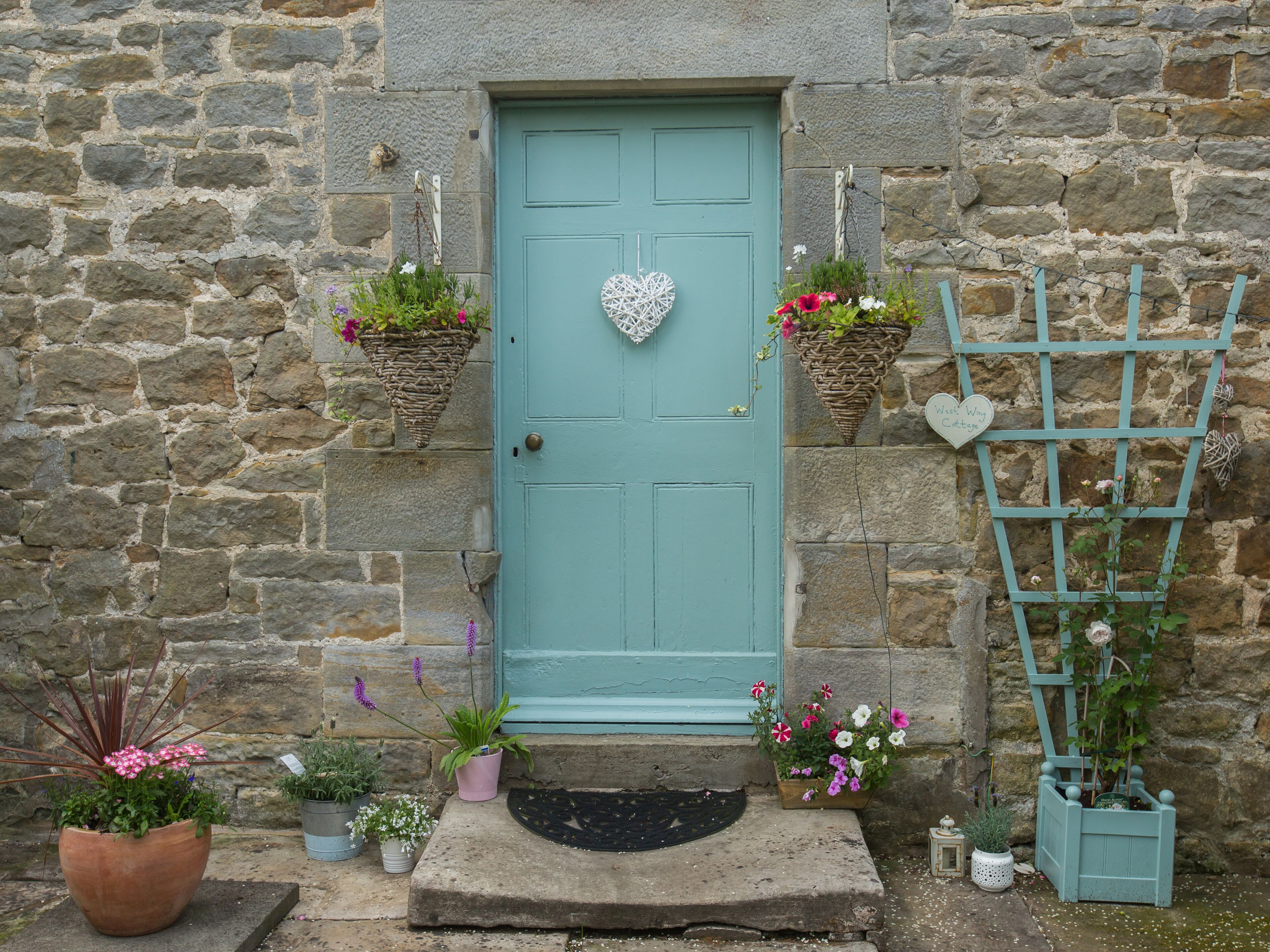 A stone building with a teal door, potted plants, and a heart-shaped decoration.