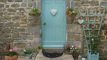 A stone building with a teal door, potted plants, and a heart-shaped decoration.