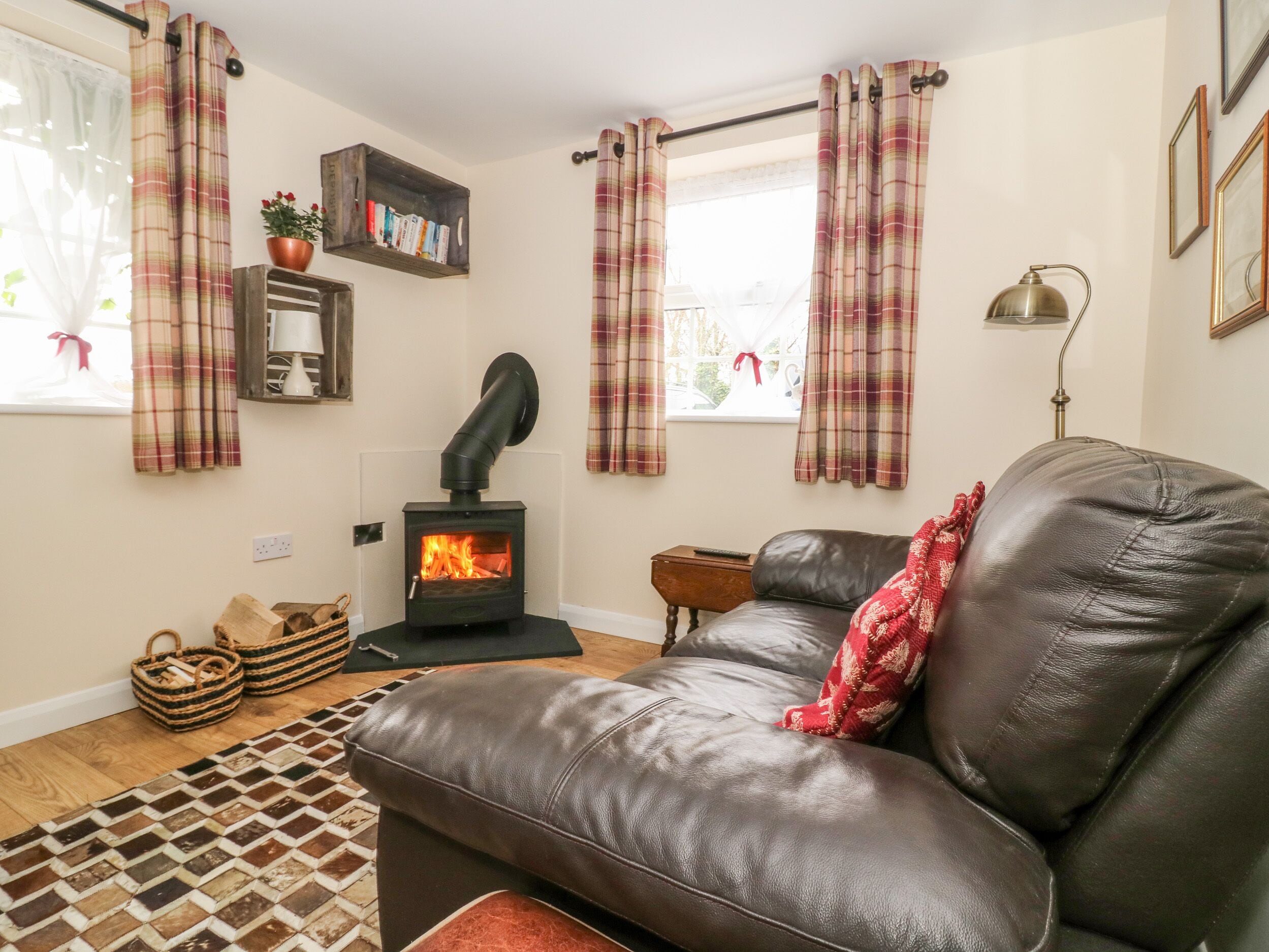 A cozy living room with a leather sofa, a fireplace, a bookshelf, and plaid curtains.