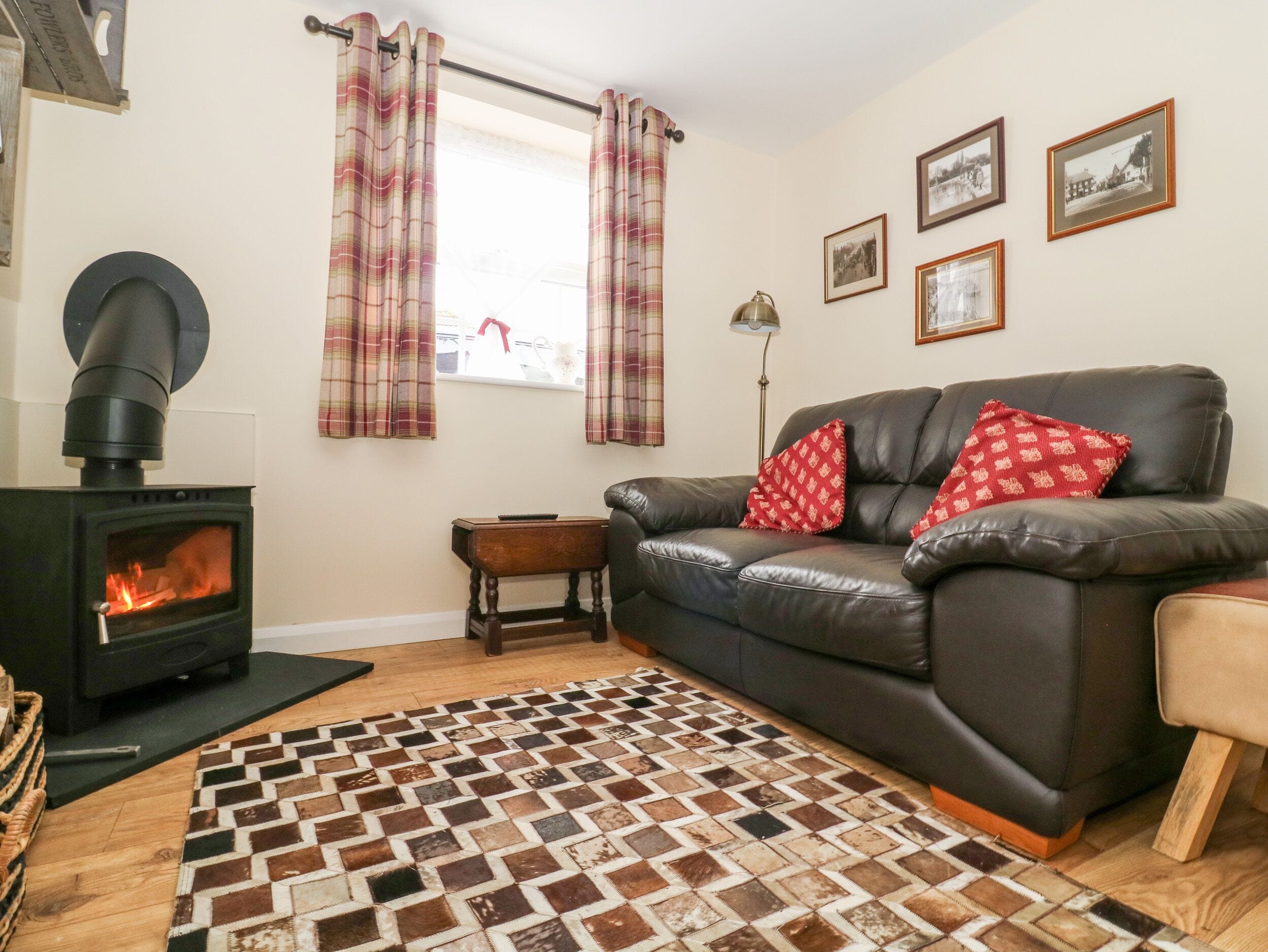 A cozy living room with a fireplace, a leather sofa, plaid curtains, and a patterned rug.