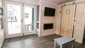 A room with a wooden floor, a bench, a fireplace, a TV mounted on the wall, and a sliding door. - Old Joiners Shop (Saltburn-by-the-Sea)