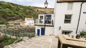 A stone staircase leading to a white building with a blue door, a wooden table with a pitcher and glasses, and a lamp post. - Old Joiners Shop (Saltburn-by-the-Sea)